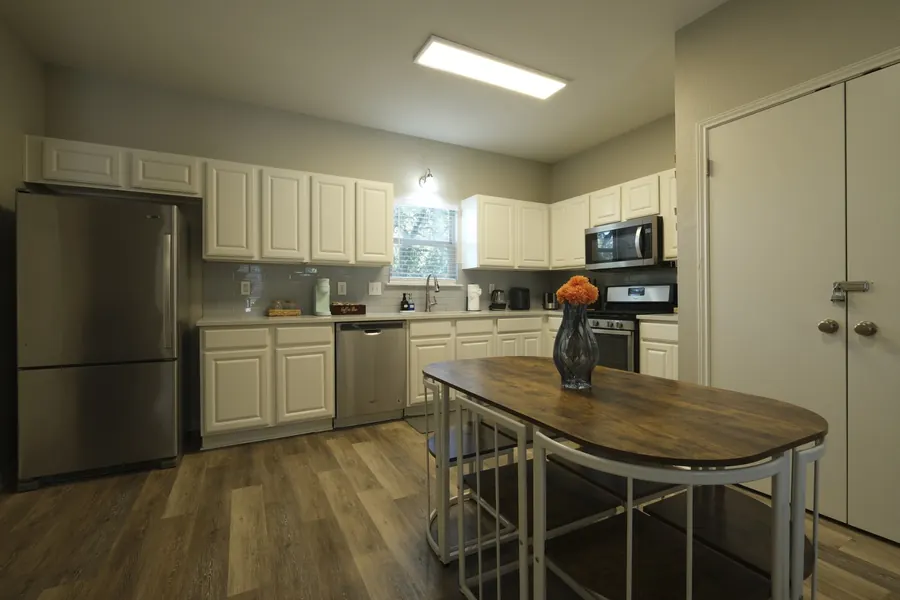 The same kitchen straight out of camera — heavy yellow cast from a linear ceiling troffer, blocked shadows under the cabinets.