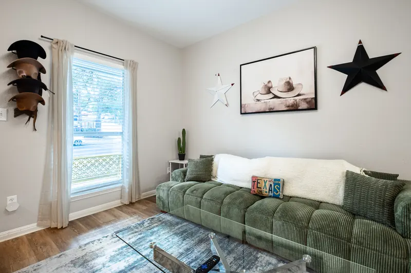 Green sofa beside a curtained window, daylight falling across the rug.
