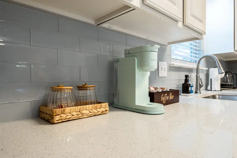 Coffee bar detail — sage green machine, woven tray and sink on a quartz counter.