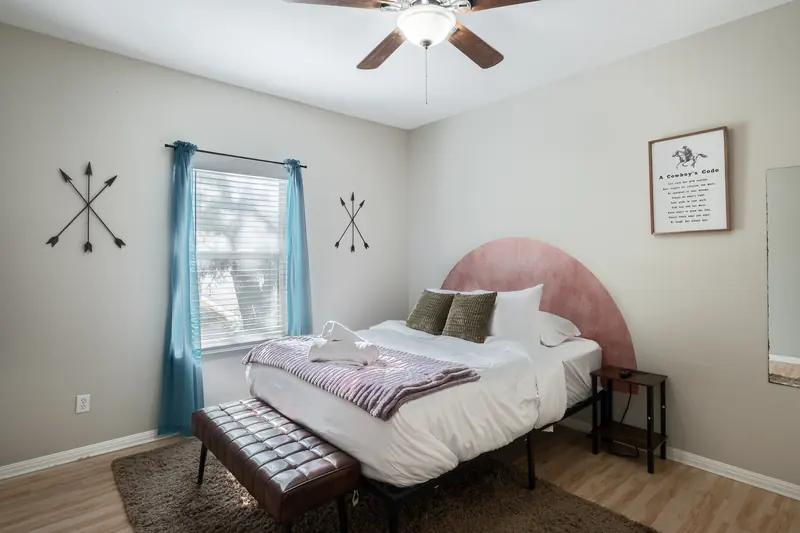 Bedroom with a pink arched headboard, blue curtains and folded towels on white bedding.