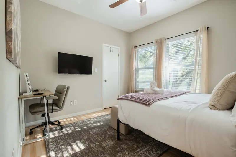 Guest bedroom with a desk and chair, television on the wall, twin window light.