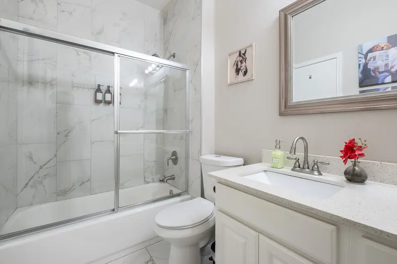 Full bath with a glass shower screen, marble tile and a white vanity.