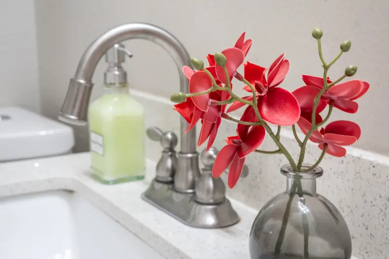 Chrome faucet with a small vase of red flowers on a bathroom counter.