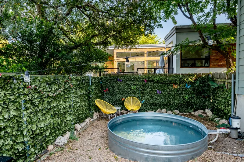 Galvanised stock-tank pool in a gravel yard with yellow chairs and an ivy screen.