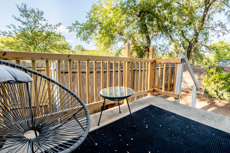 Upper timber deck with a black mat, round table and a hanging chair frame.