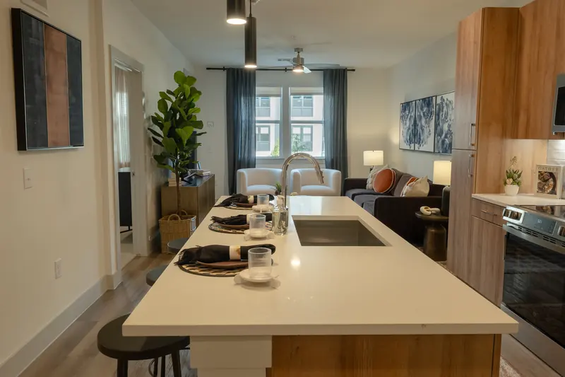 Model apartment kitchen island with stools, dining table and living area beyond.