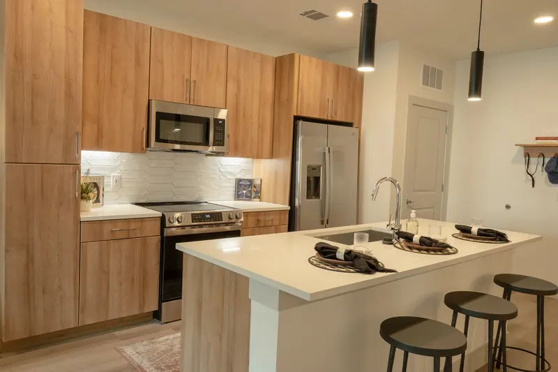 Light oak kitchen with quartz counters, stainless range and pendant lights.