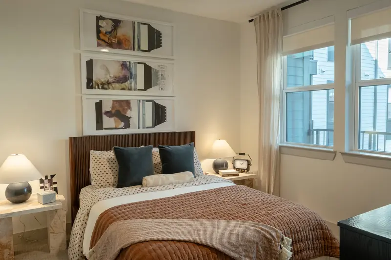 Bedroom from the doorway, bed styled with layered linens beside a bright window.